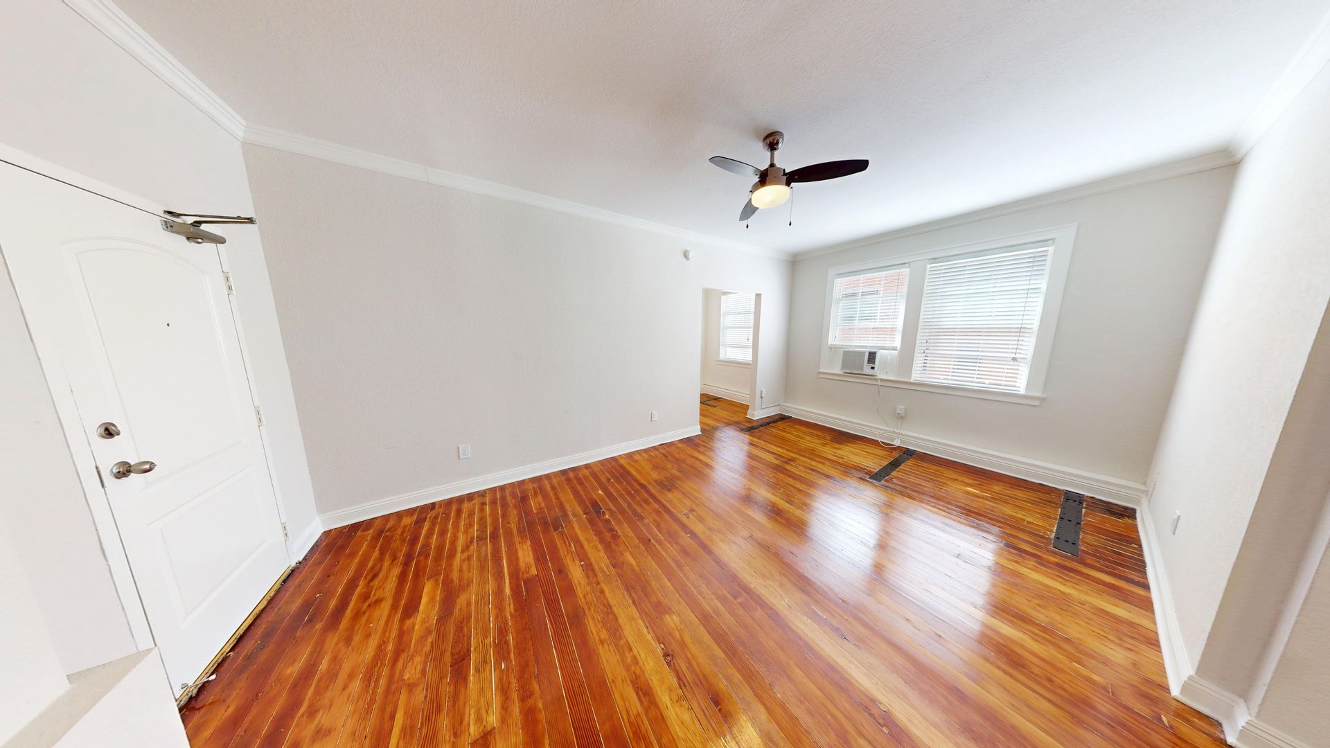 Empty living room with hardwood floors, white walls, and a ceiling fan.