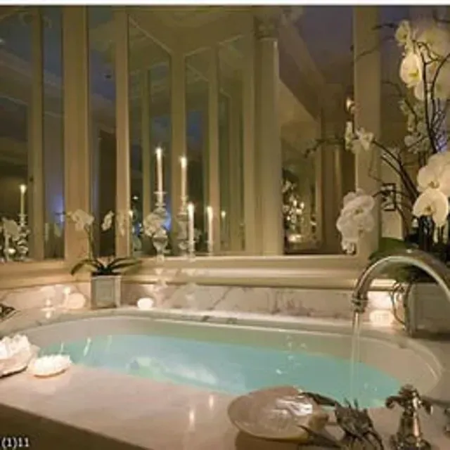 Luxurious marble bathroom with a lit bathtub, candles, flowers, and columns.