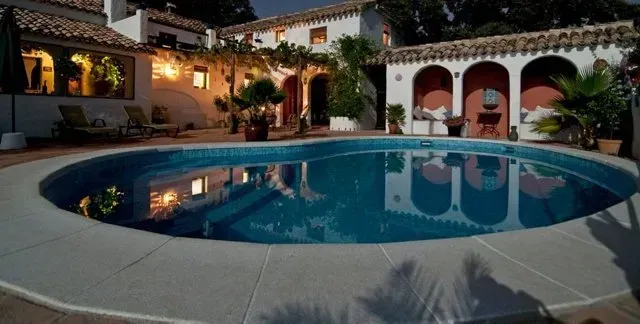 Pool in front of a Spanish-style house at dusk. Arches, lights, and water reflections.