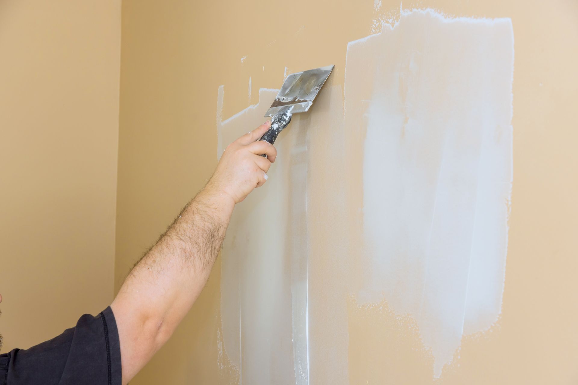 Person using a putty knife to apply drywall compound to a beige wall. Person using a putty knife to apply drywall compound to a beige wall.