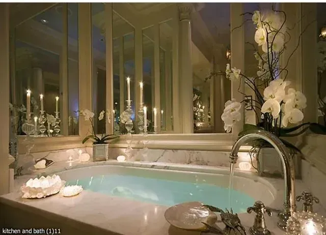 Luxurious bathroom with a bathtub, marble surfaces, and candlelit mirrors.