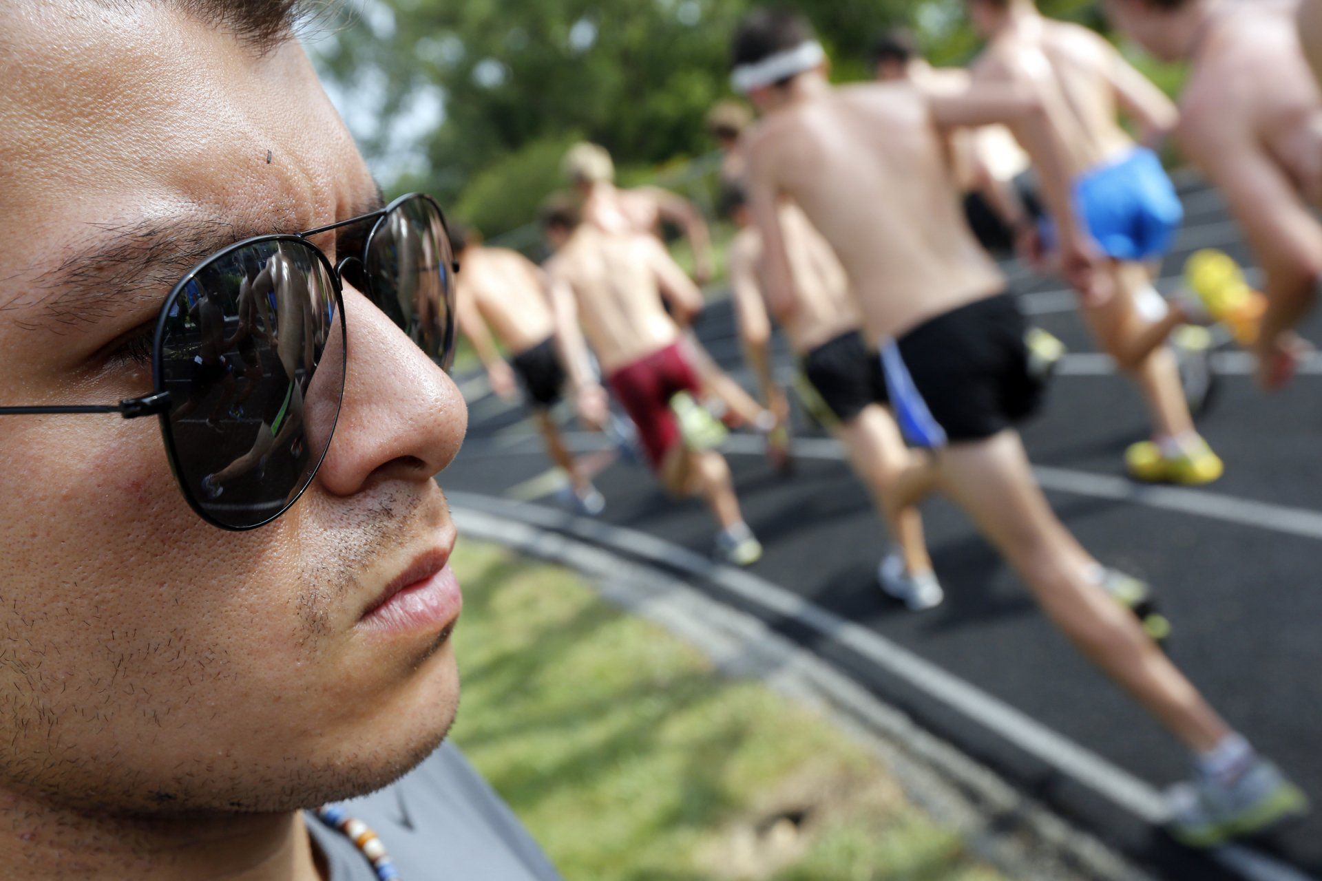 A man wearing sunglasses looks at a group of people running on a track
