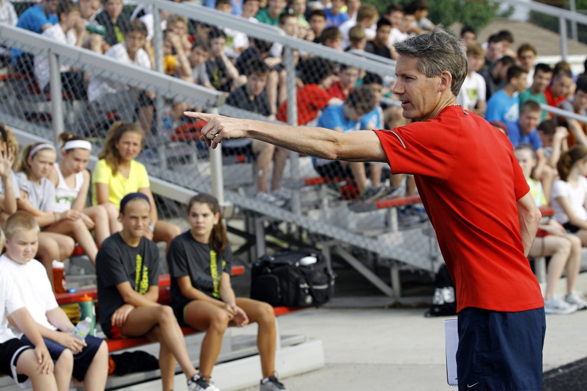 A man in a red shirt is pointing at a crowd of people sitting in the stands.