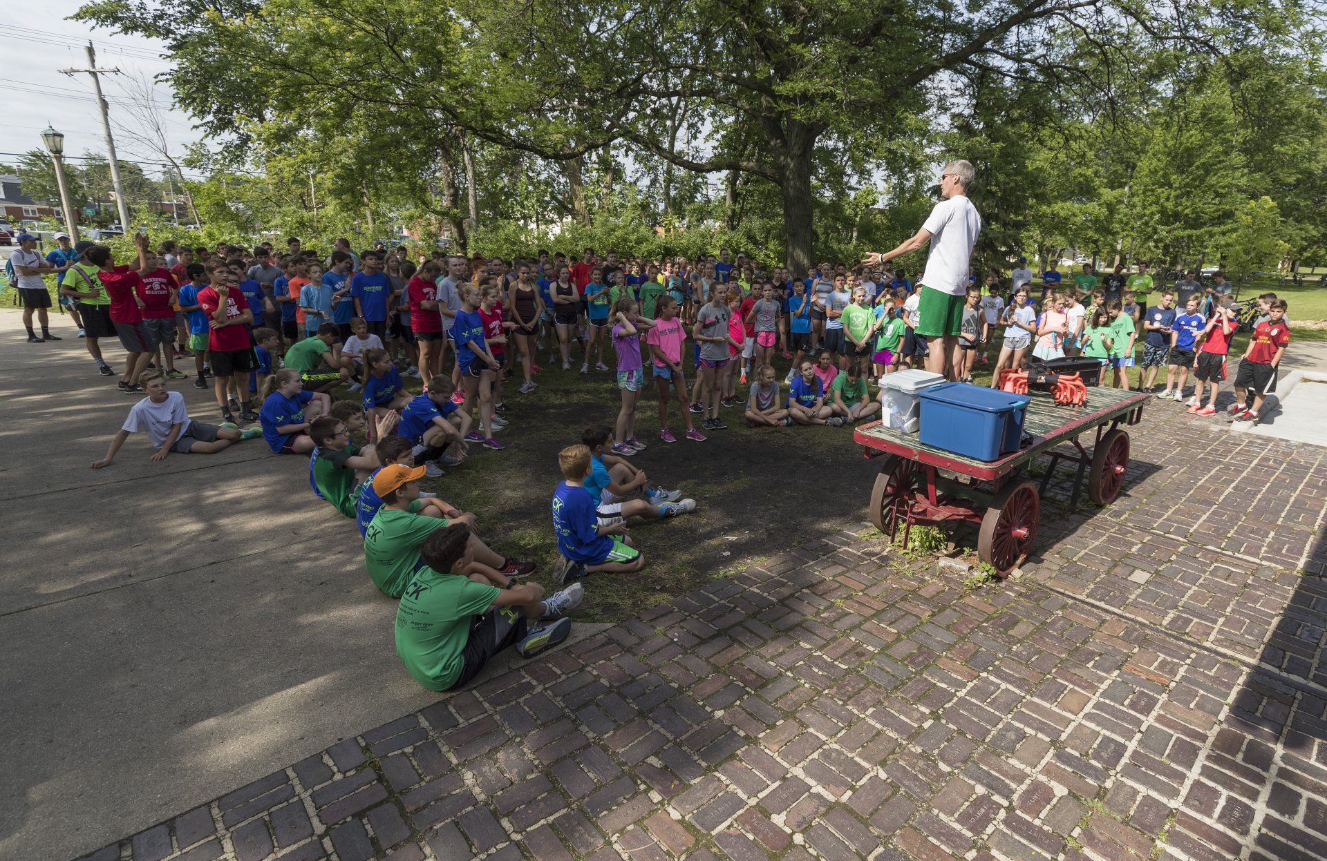 A man is standing on a wagon talking to a group of children.