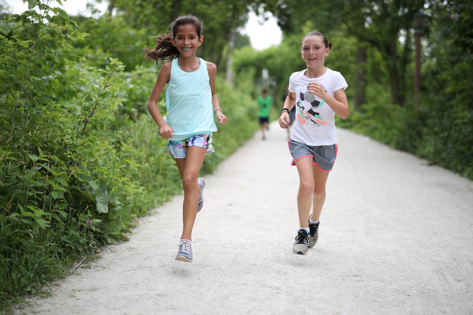 Two young girls are running down a dirt path.
