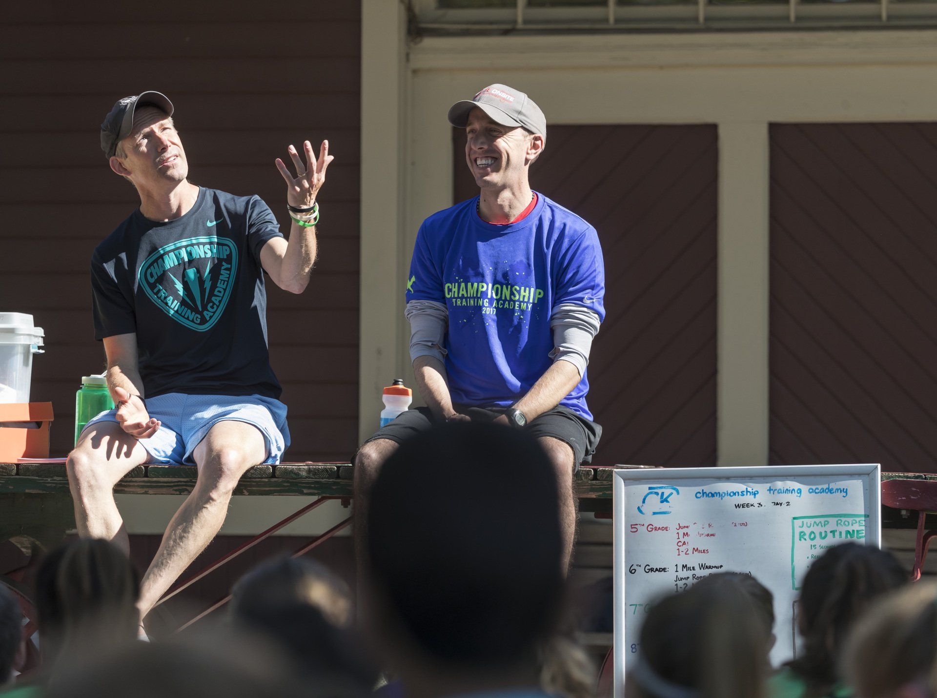 Two men are sitting on a stage in front of a crowd and one of them is wearing a blue shirt that says california