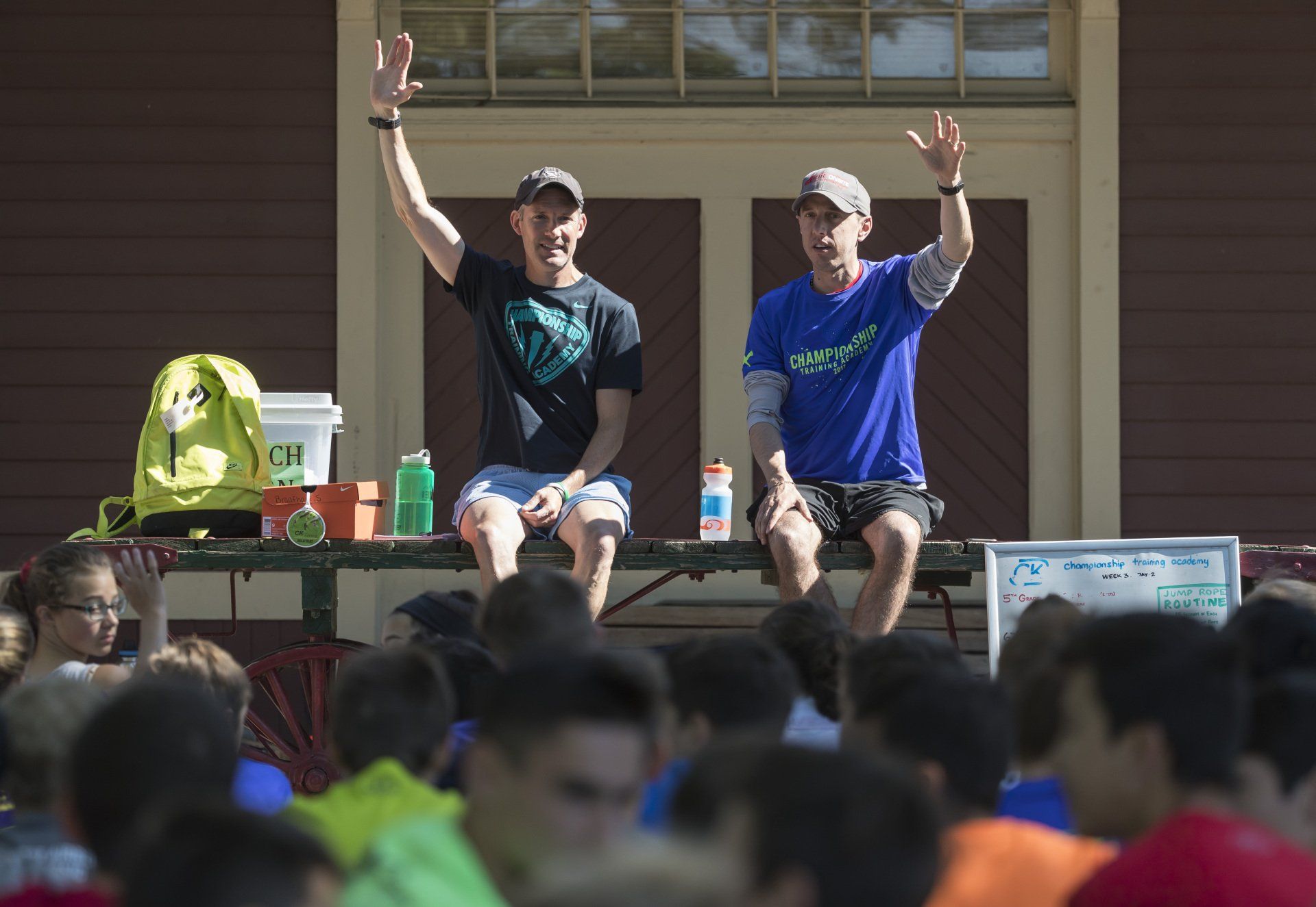 Two men are sitting on a picnic table with their hands in the air.