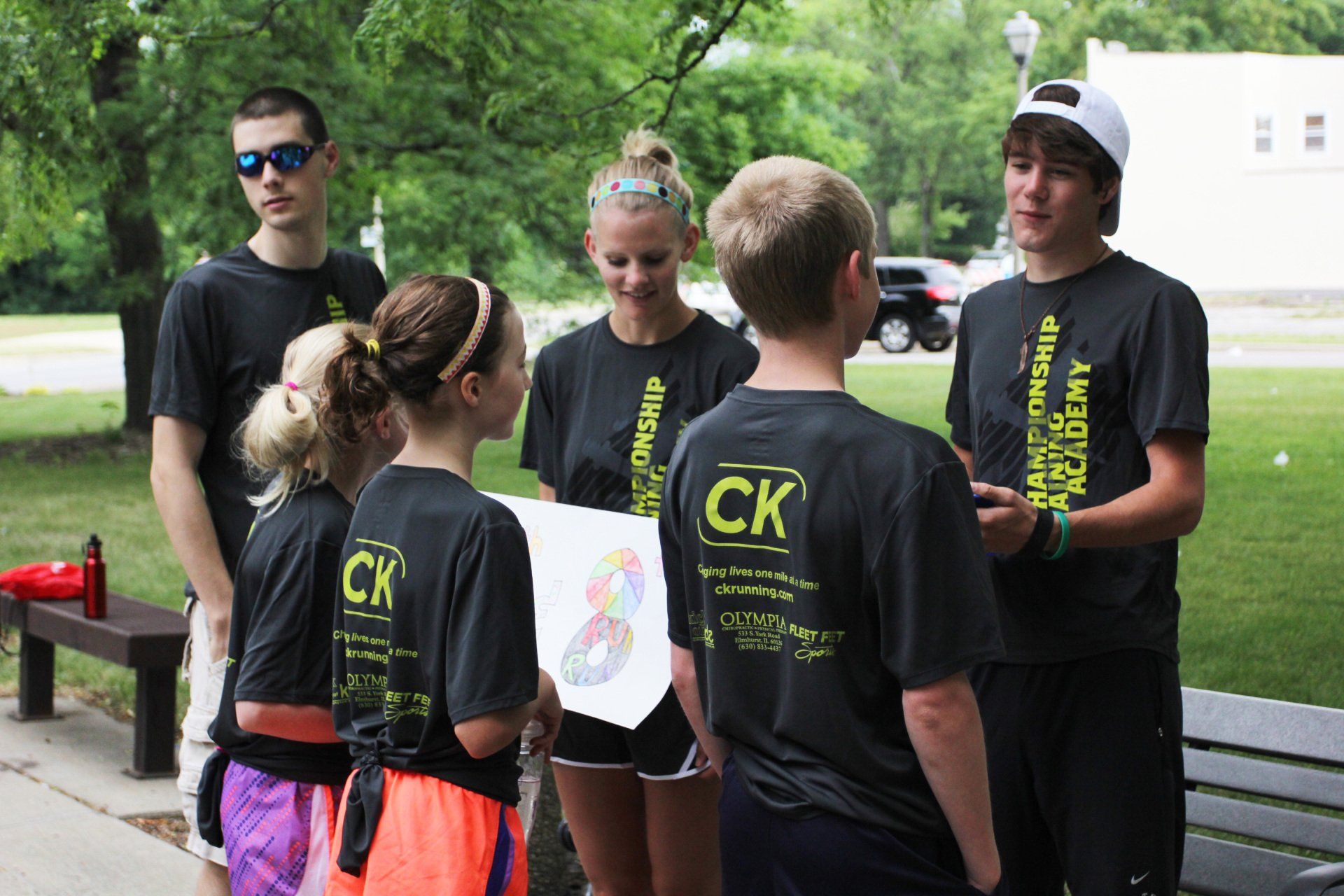 A group of young people wearing ck shirts are standing around a bench.