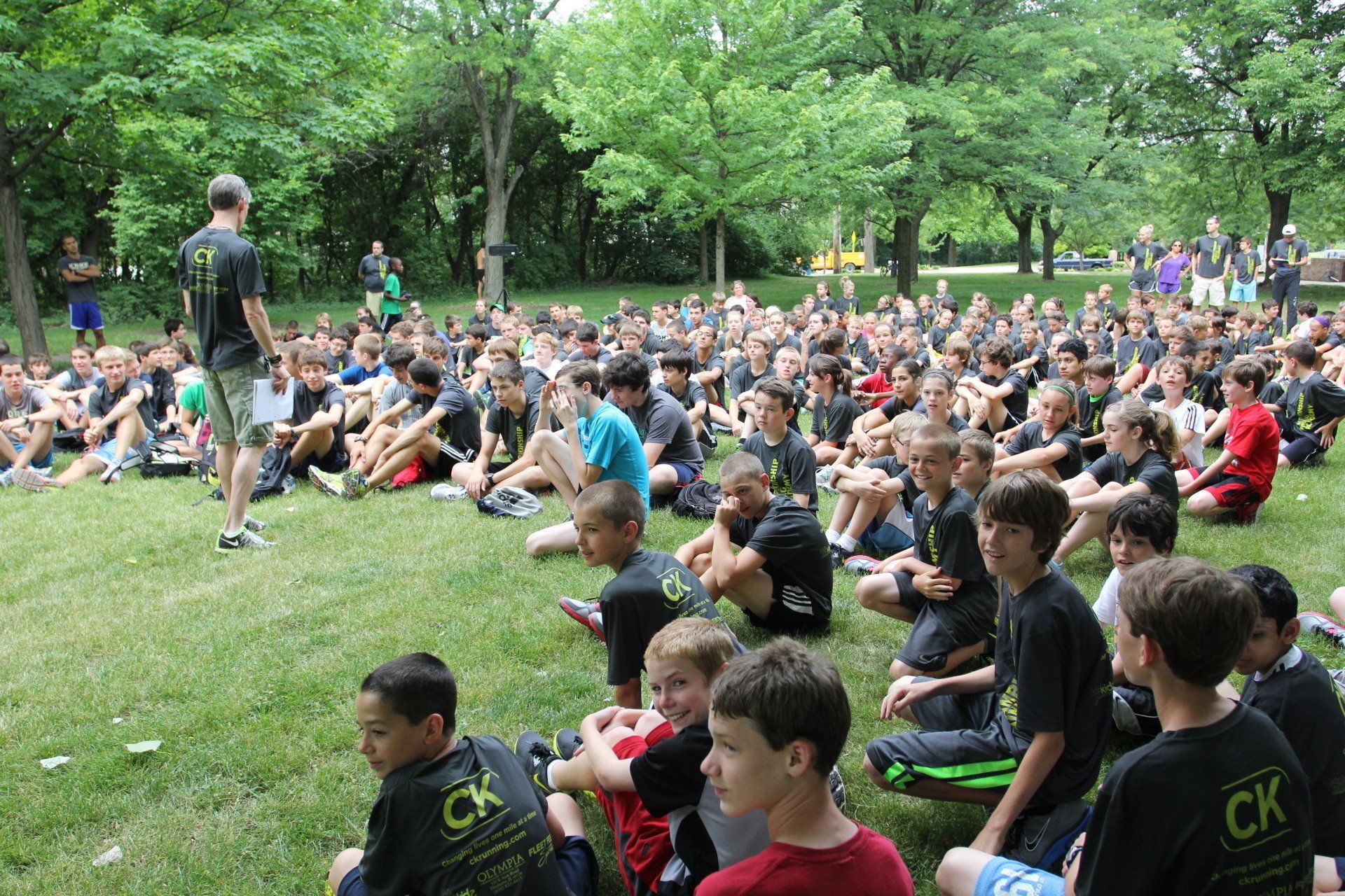 A large group of children are sitting in the grass wearing ck shirts