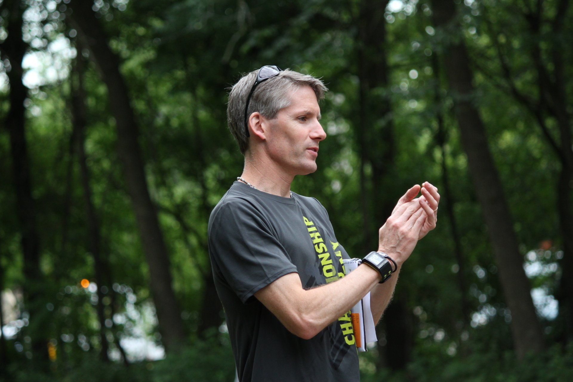 A man in a black shirt is clapping his hands in the woods.