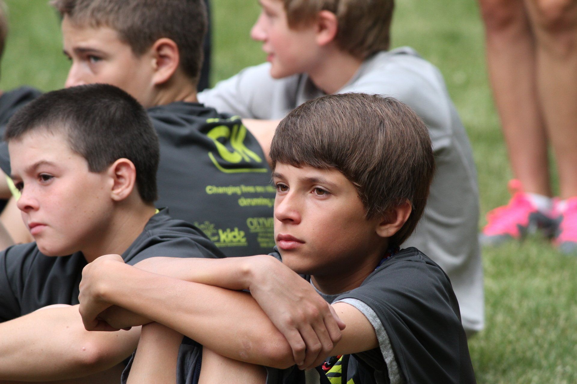 A group of young boys are sitting on the grass with their arms crossed.