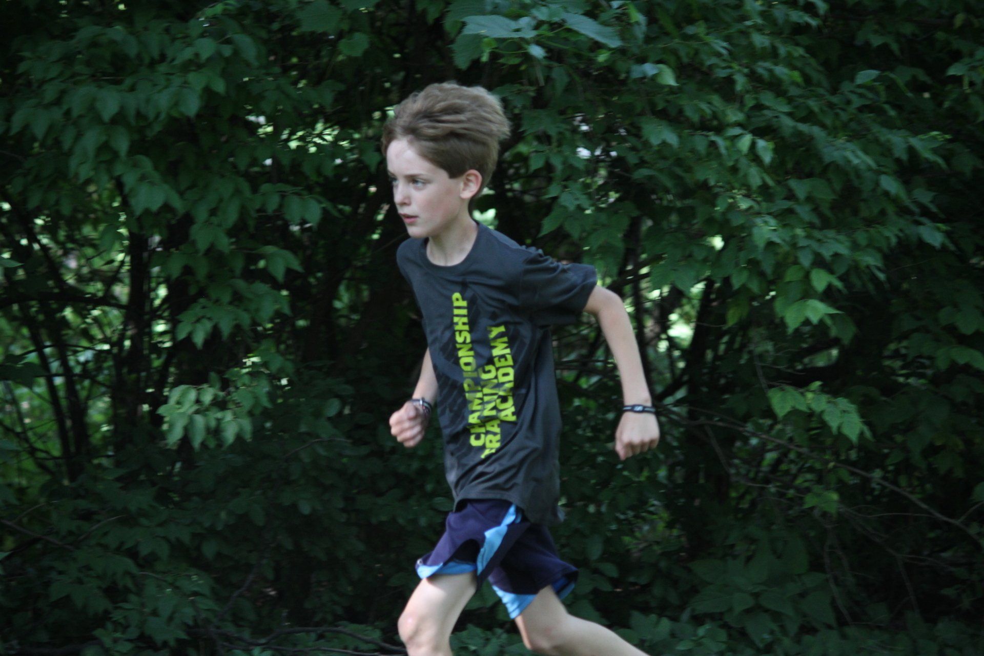 A young boy is running through the woods wearing a t-shirt that says championship