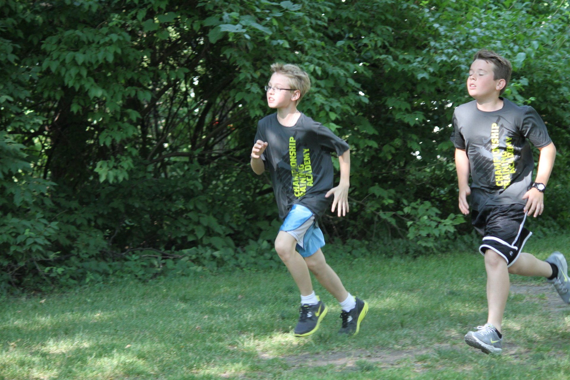 Two young boys are running in a park.