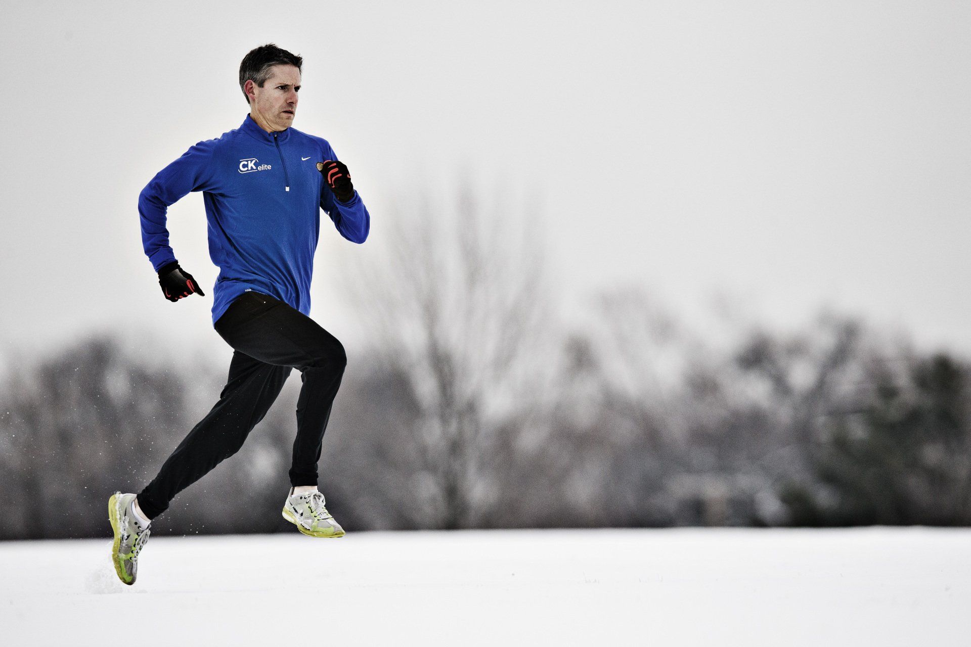 A man in a blue shirt is running in the snow.