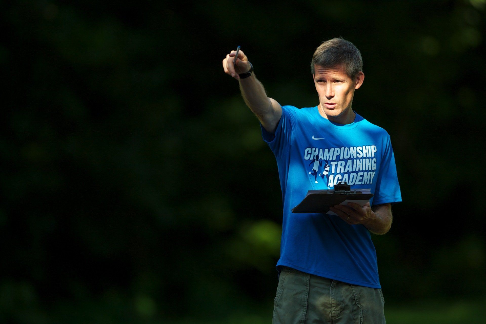 A man in a blue shirt is holding a clipboard and pointing.