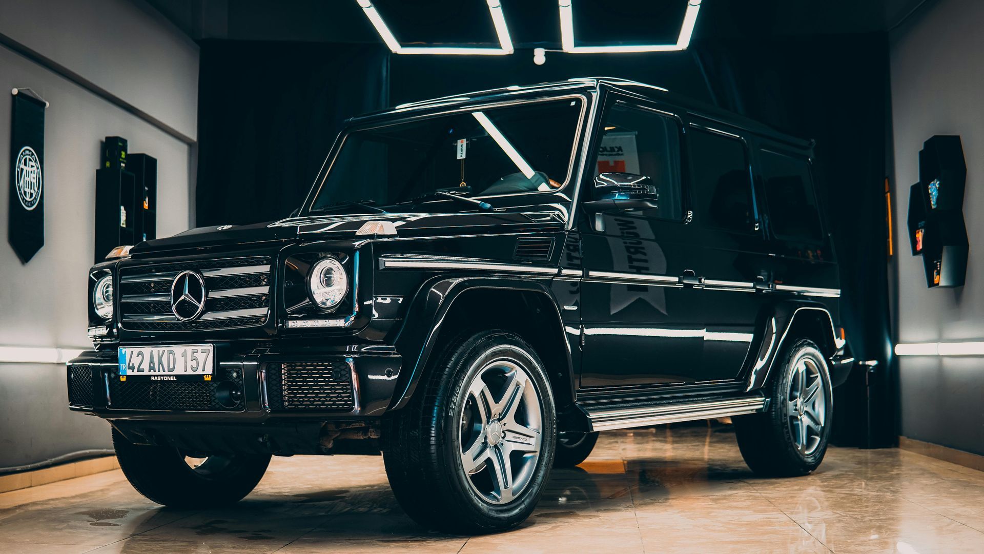 Black Mercedes-Benz G-Wagon SUV parked in a brightly lit garage, with silver rims and license plate visible.