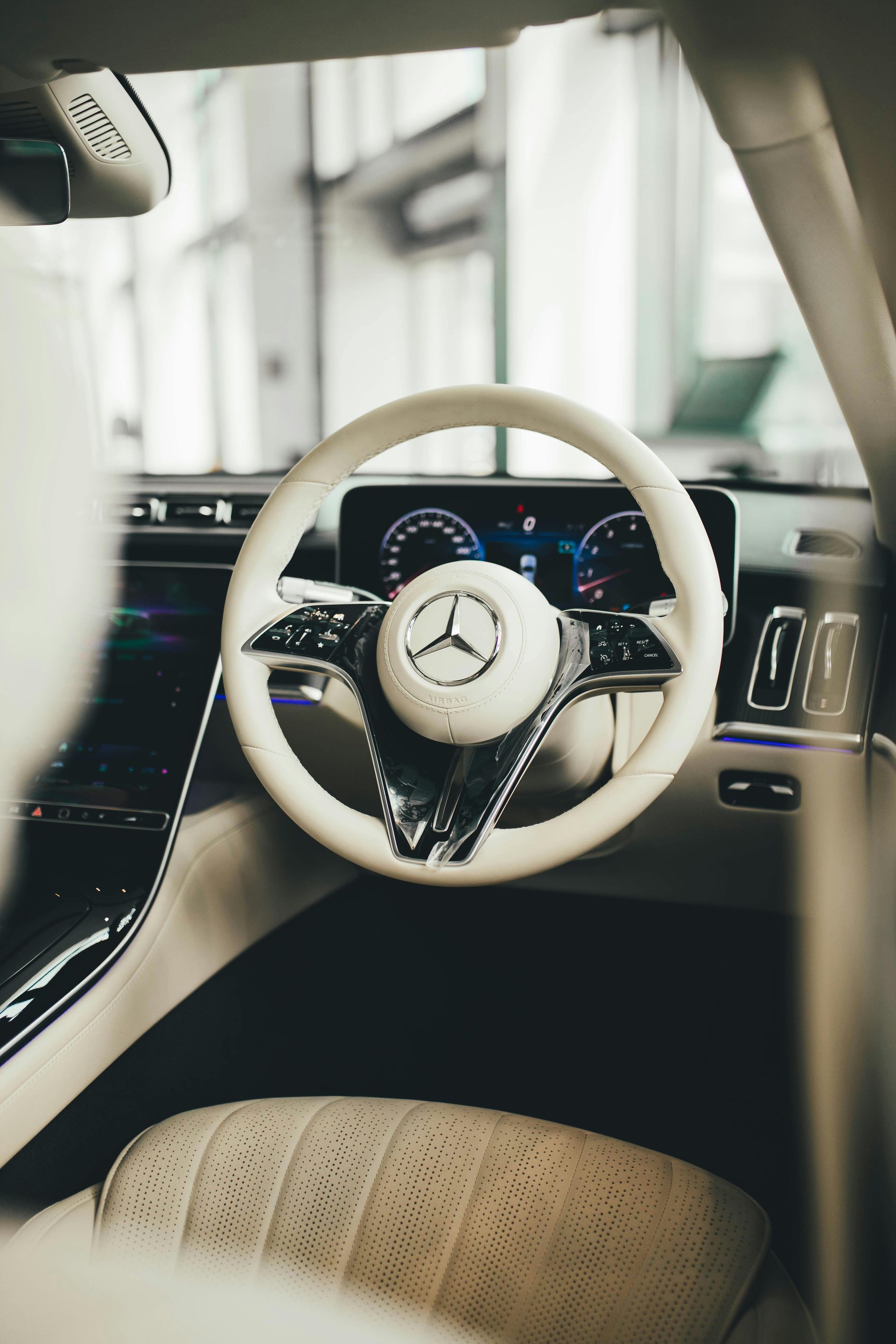 Interior view of a white Mercedes car with a white steering wheel and a digital dashboard.