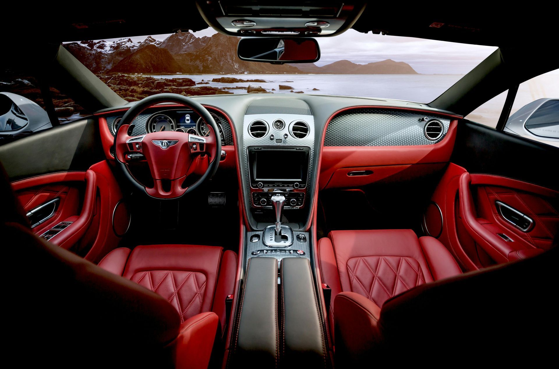 Red leather interior of a luxury car with a view of the sea and mountains.