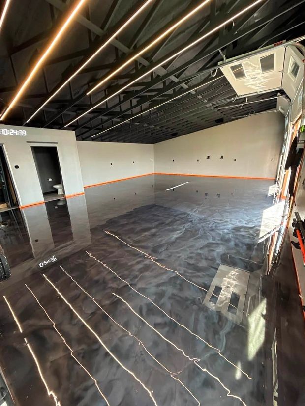 Empty unfinished room with glossy black floor, exposed ceiling, and white walls with orange trim