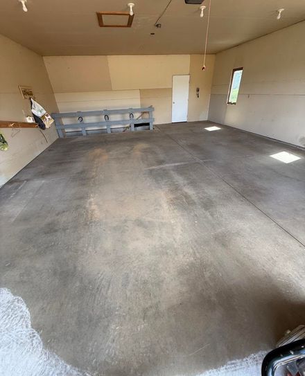 Empty garage with concrete floor, shelving on the left, and a side door and window on the right.