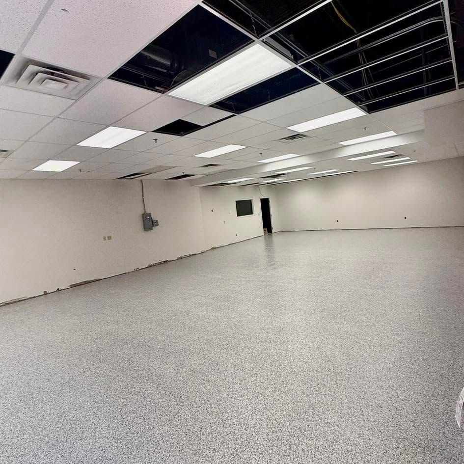 Empty office room with white walls, speckled floor, and damaged drop ceiling panels exposed