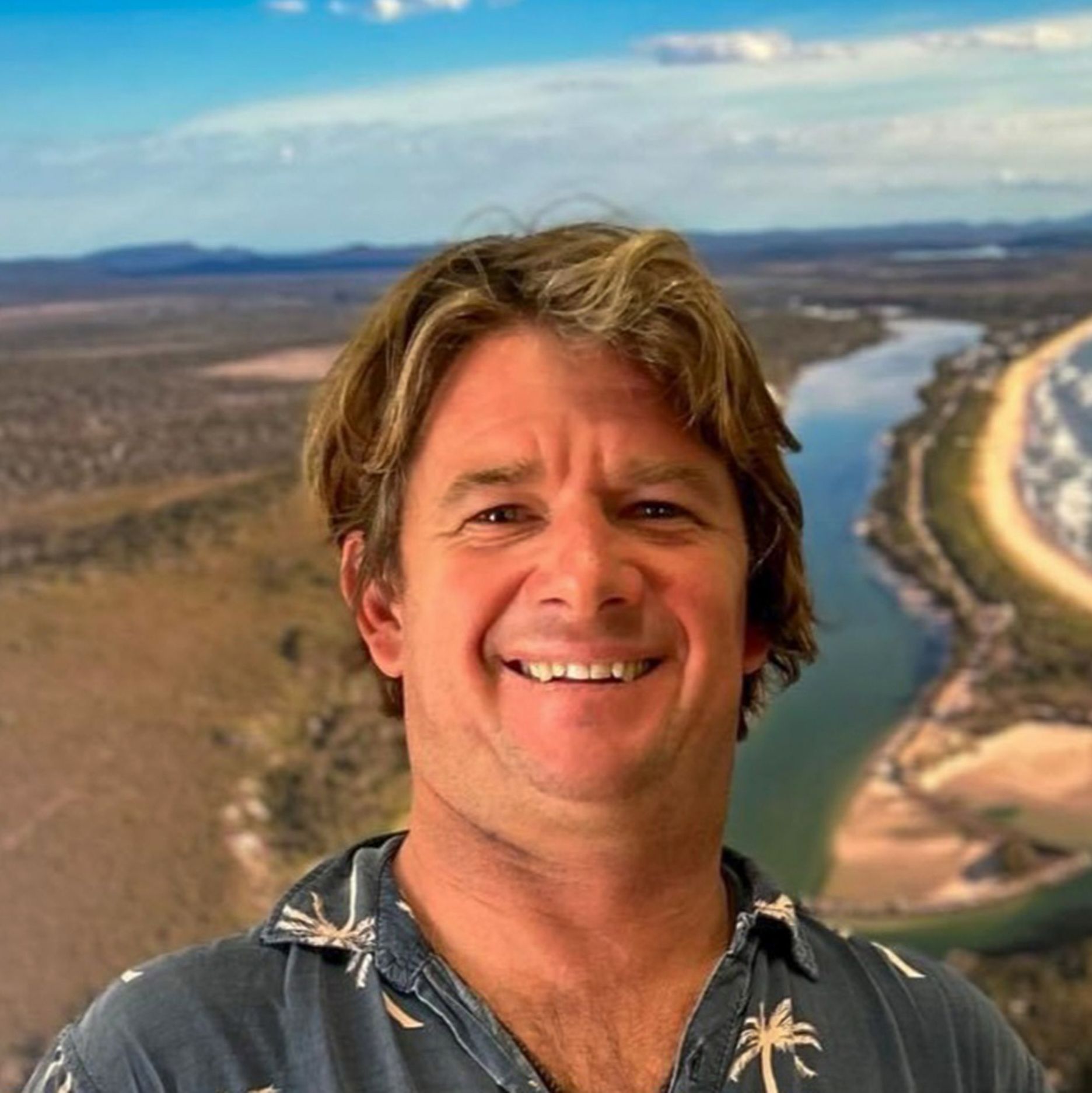 Bust shot of smiling man standing in front of scenic photo