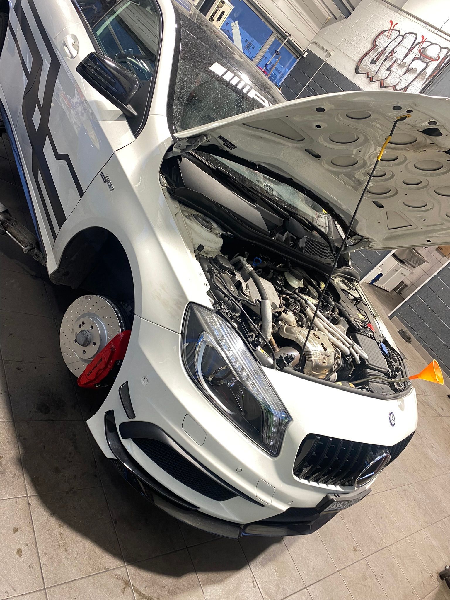 Une voiture blanche avec le capot ouvert est garée dans un garage.
