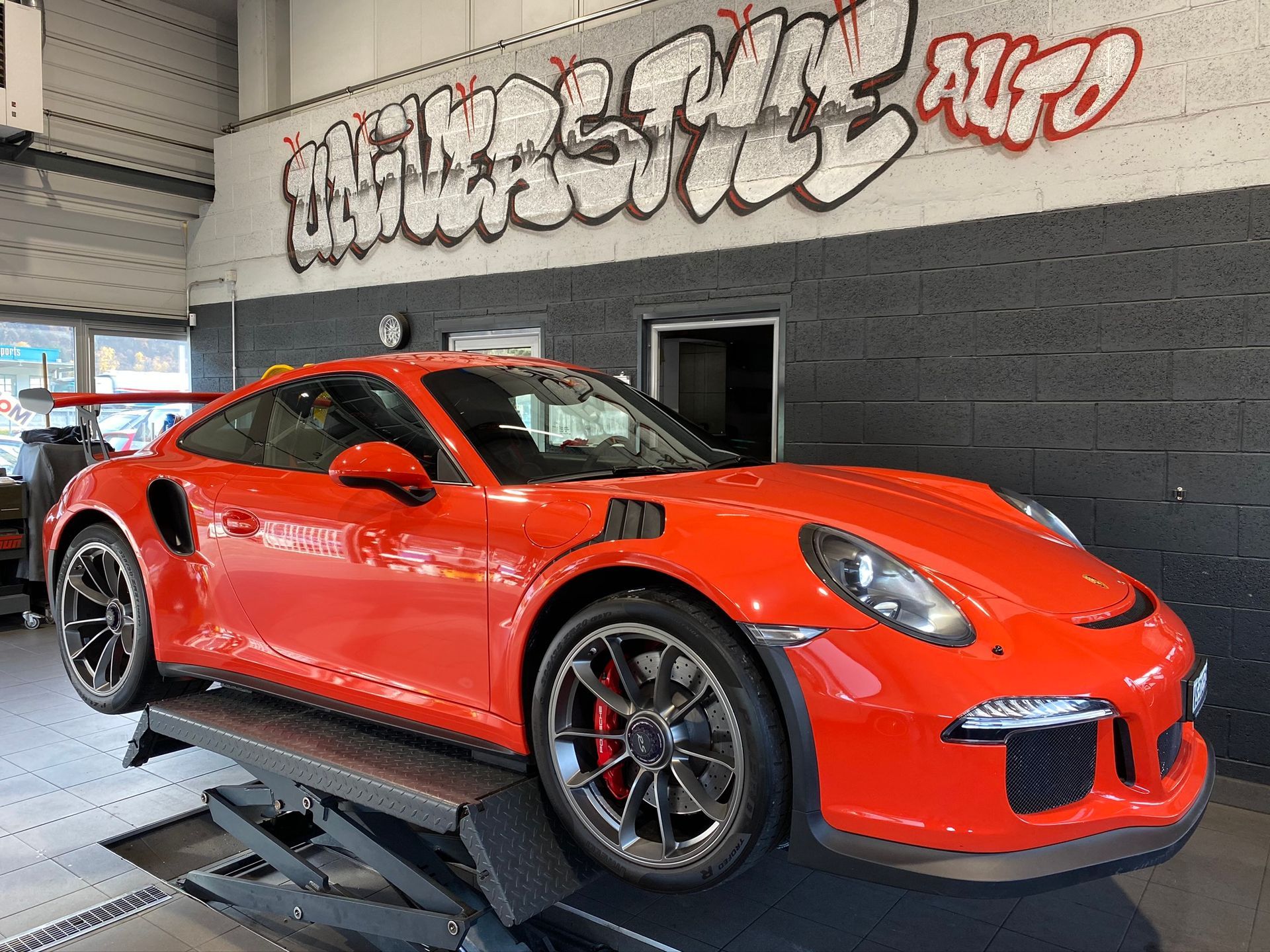 Une Porsche 911 GT3 RS rouge est posée sur un ascenseur dans un garage.