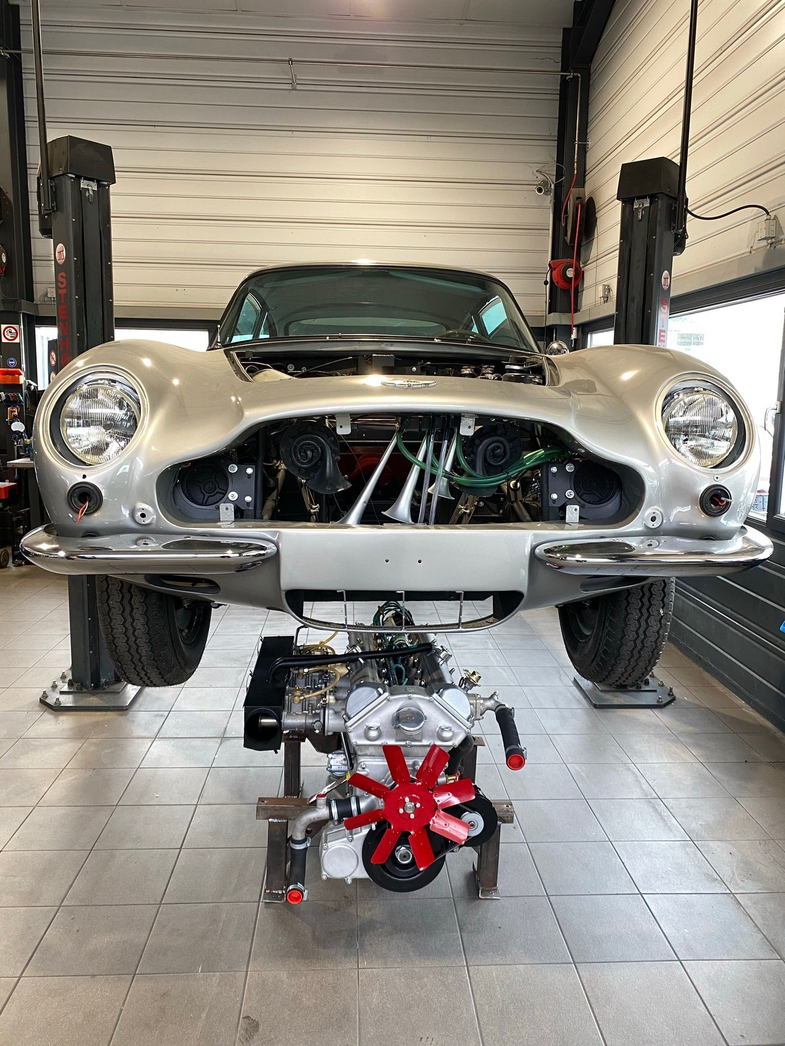 Une voiture argentée est posée sur un ascenseur avec le moteur exposé.
