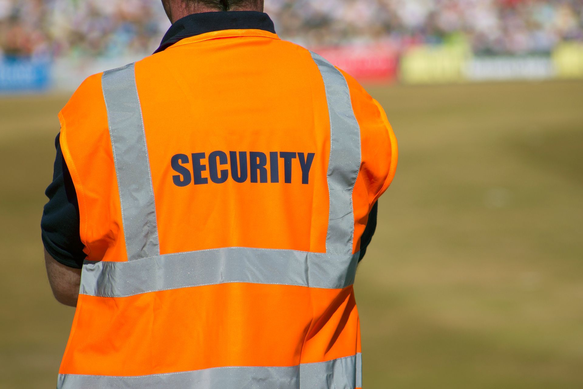 Security guard in bright orange vest, standing watch in a stadium.