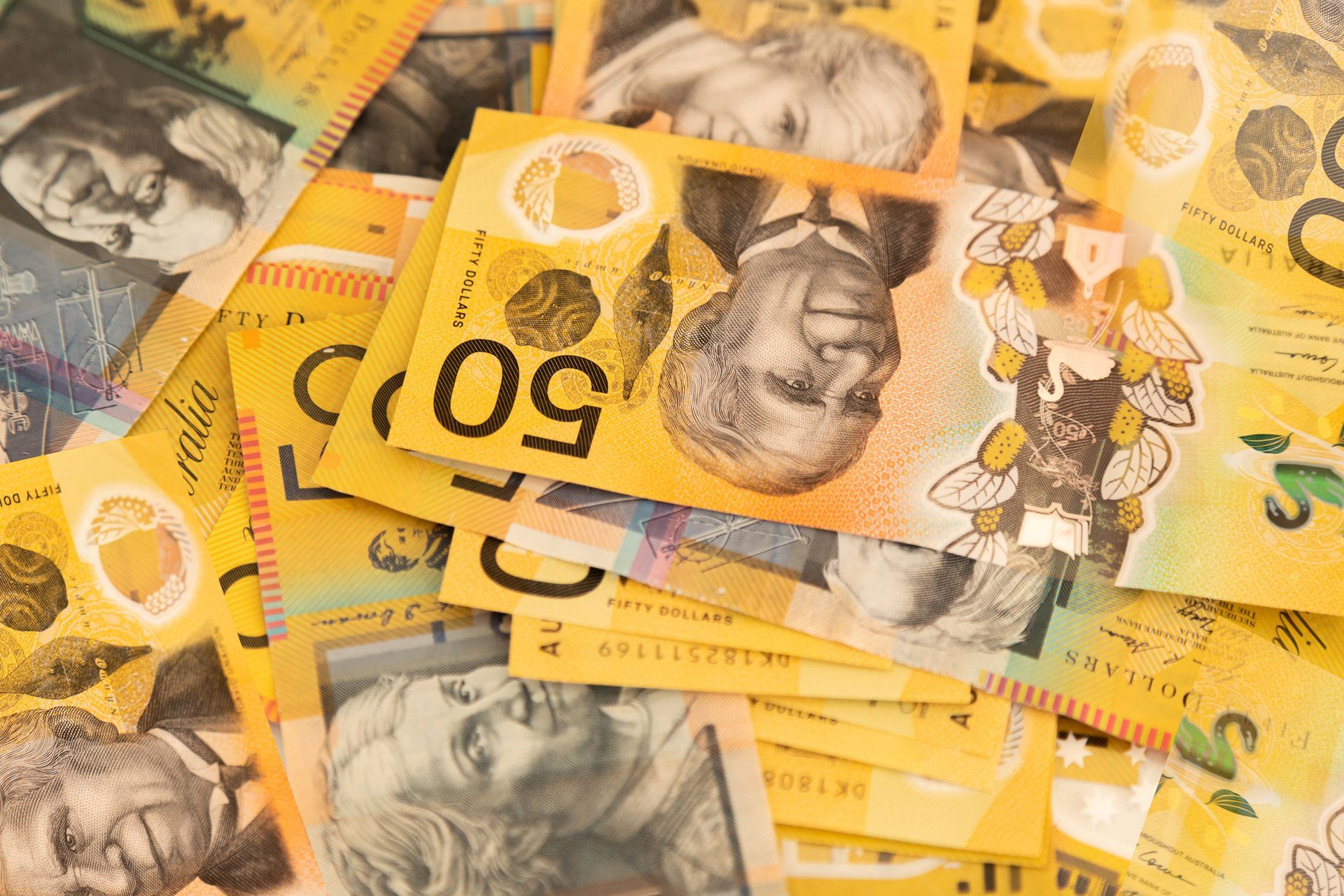 Australian fifty-dollar banknotes scattered randomly, yellow and other colors, showing prominent portraits.