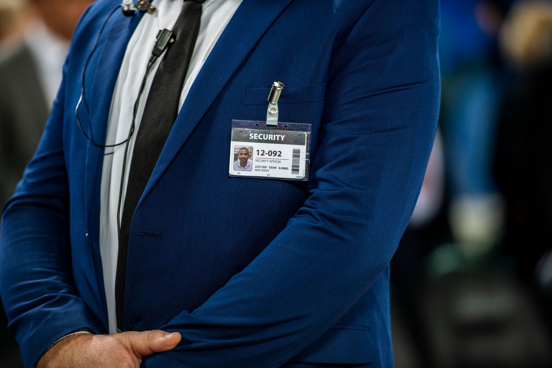 Man in a blue suit with a name badge, microphone, and black tie.
