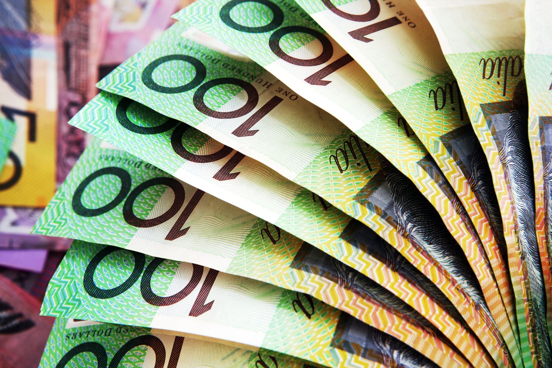 Fan of Australian $100 banknotes, showing green and yellow colors.