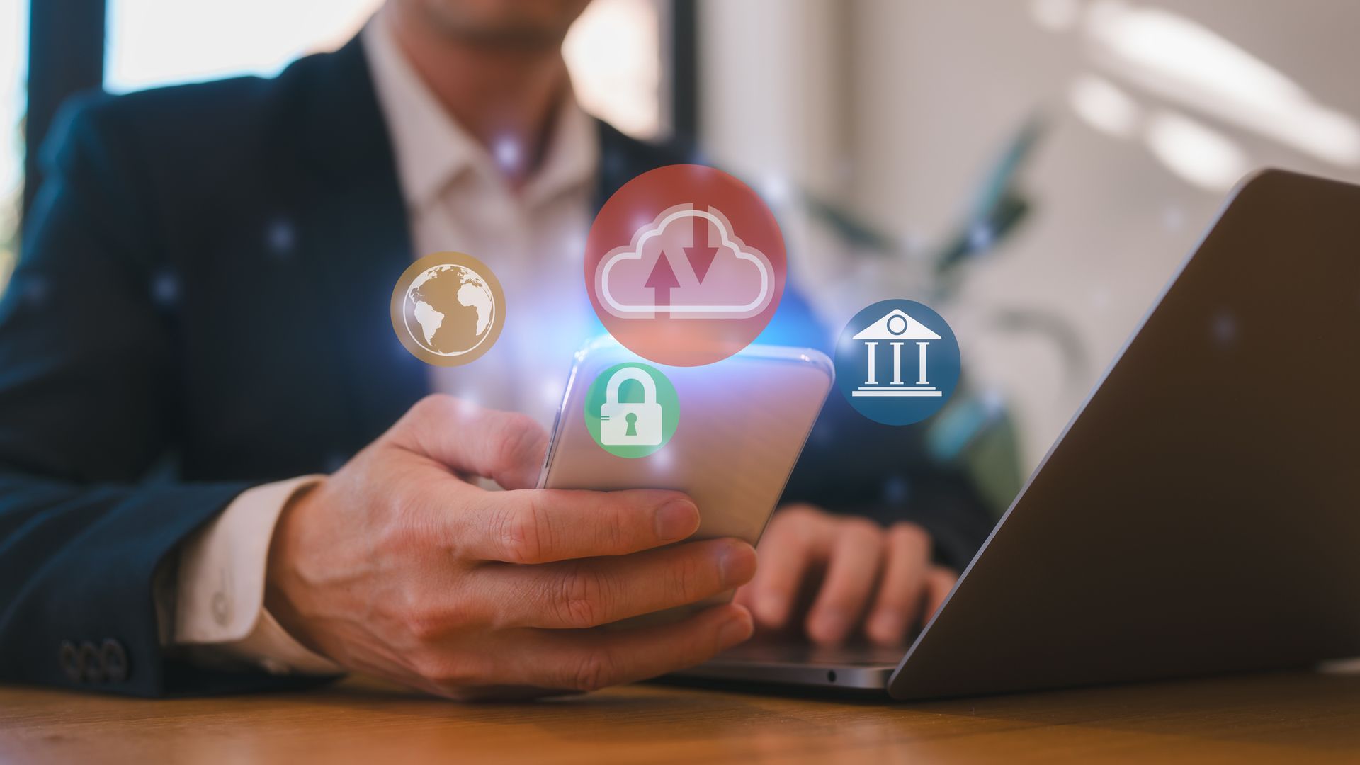 Man in suit using phone with glowing cloud, lock, bank, and globe icons overlayed. Laptop nearby.