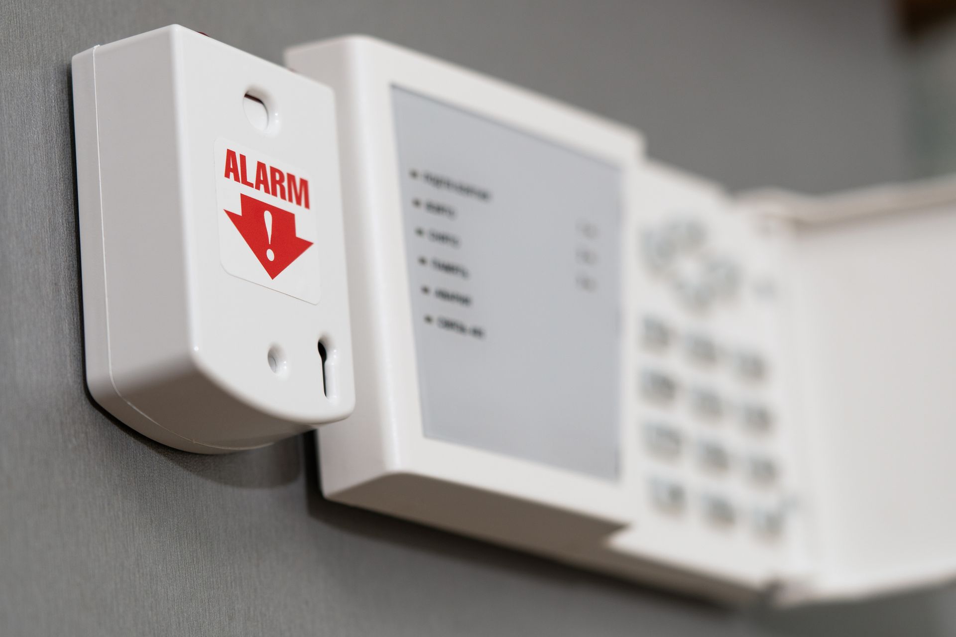 Security system control panel with alarm indicator on a grey wall.