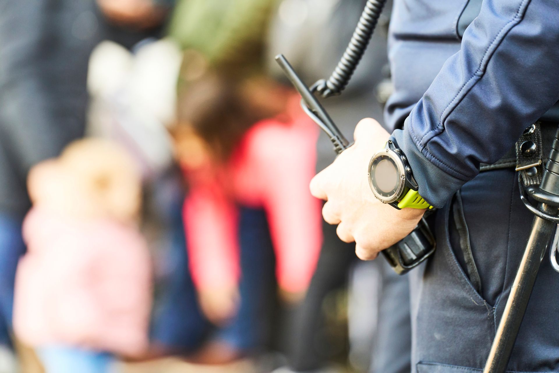 Police officer holding a radio with a crowd of people in the blurred background.
