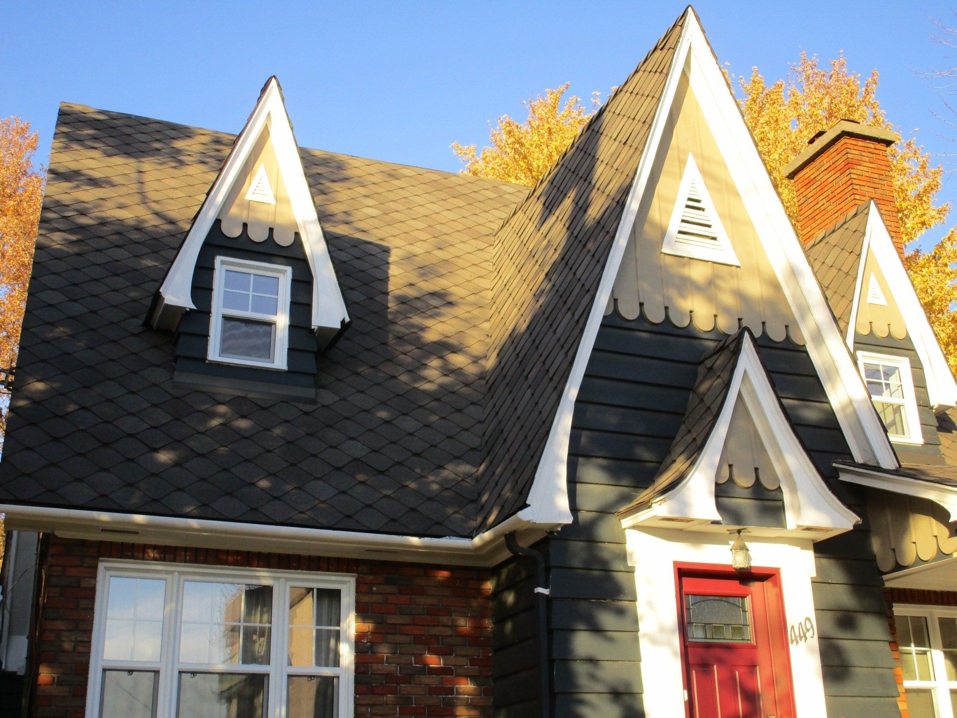 Une maison au toit à forte pente, avec des lucarnes et une porte rouge. Des feuilles d'automne en arrière-plan.