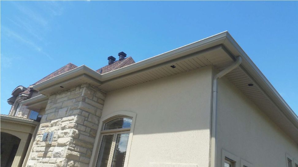 Maison en stuc beige avec façade en pierre, sous un ciel bleu clair.