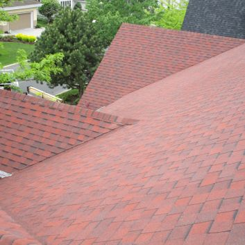 Toiture en bardeaux d'asphalte rouge d'une maison à angles multiples, dans un cadre résidentiel.