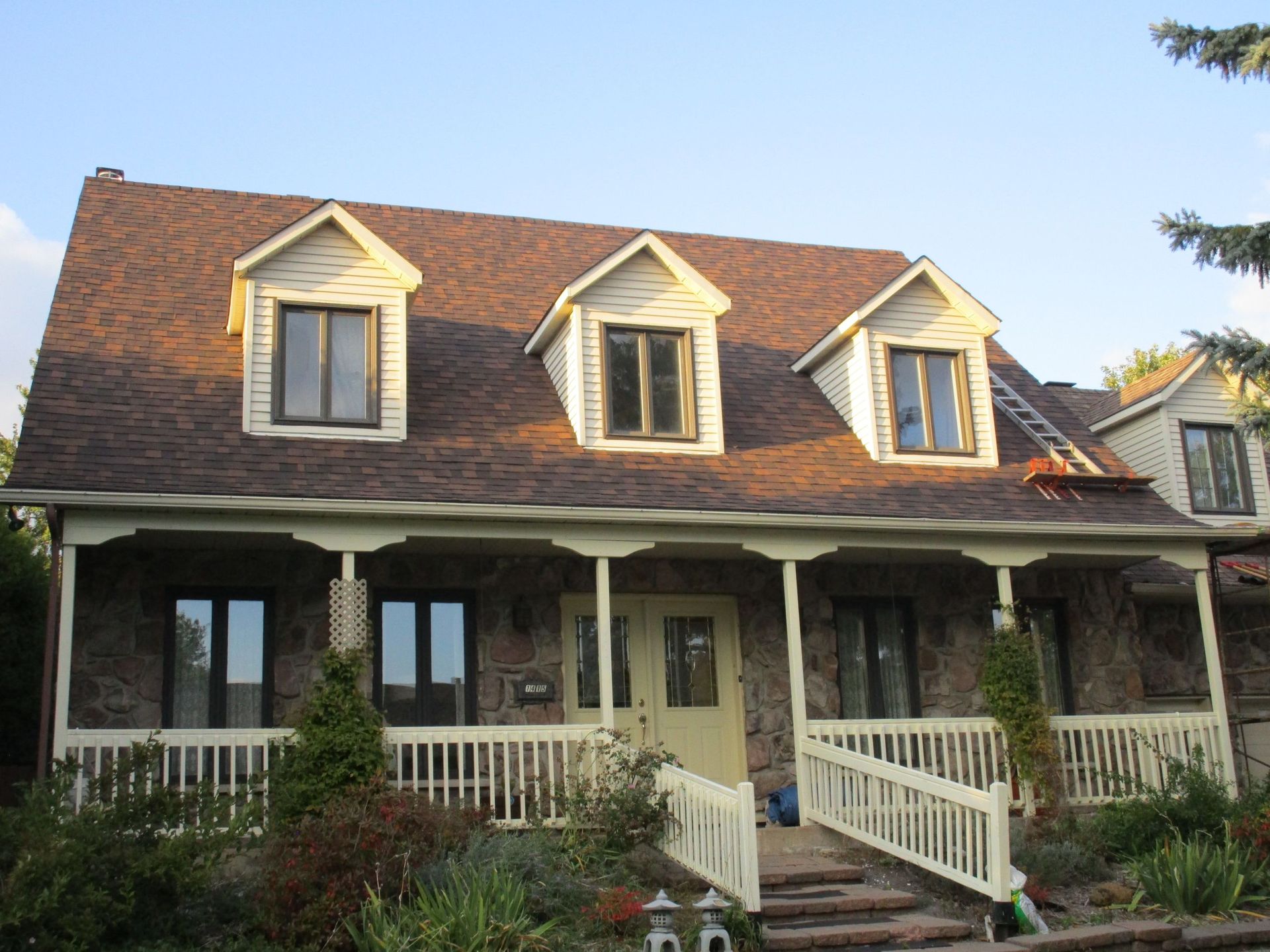 Maison en pierre avec un porche, trois lucarnes et un toit brun.