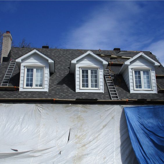 Toiture d'une maison à trois lucarnes, en construction; bâches sur le côté, échelles.