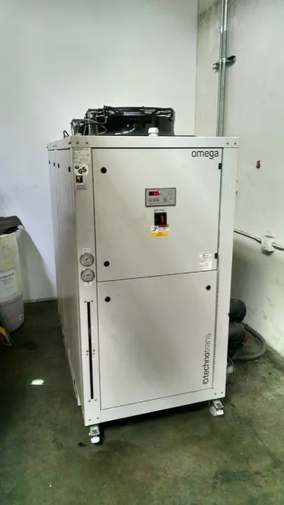 White industrial machine on casters in a room with concrete floor and pipes on the wall White industrial machine on casters in a room with concrete floor and pipes on the wall