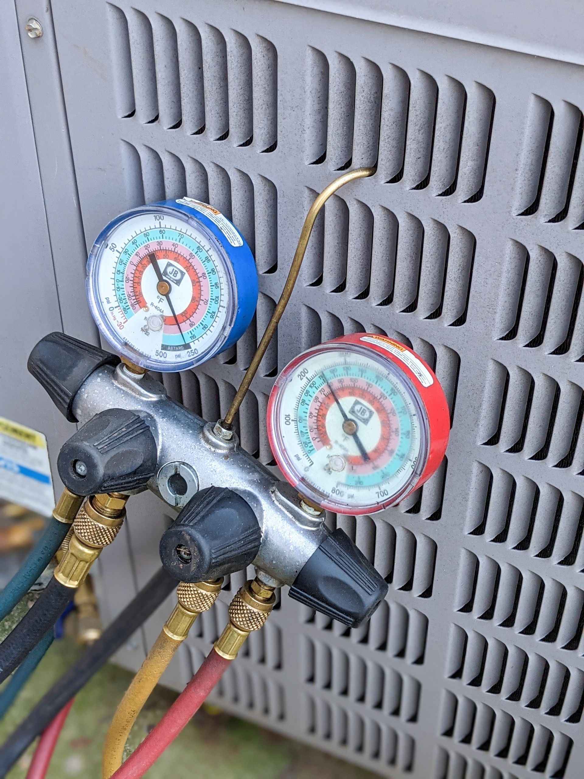 Two HVAC manifold gauges with red and blue dials attached to an outdoor unit