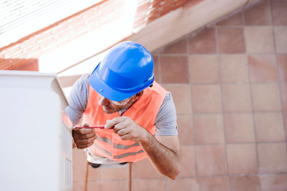 Construction worker in blue hard hat inspecting a wall with a tool on a tiled floor in a stairwell