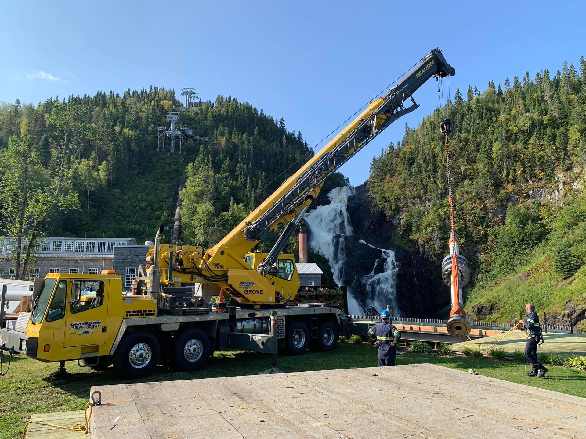 Un camion jaune avec une grue attachée est garé devant une montagne.