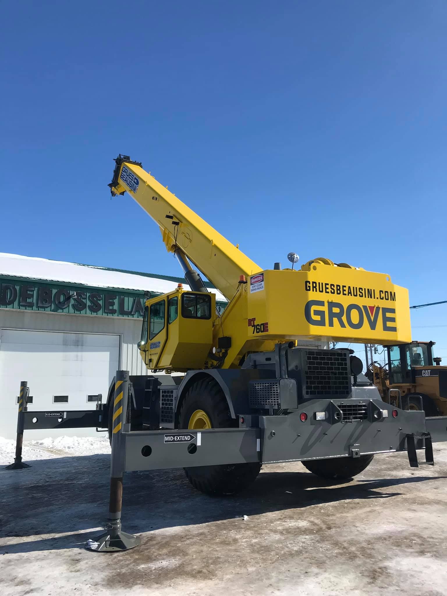 Grue mobile Yellow Grove sur châssis gris, stabilisateurs déployés, stationnée à l'extérieur sous un ciel bleu.