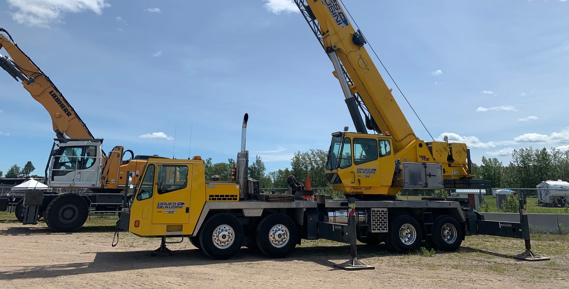 Deux camions-grues jaunes sont garés l'un à côté de l'autre dans un champ de terre.