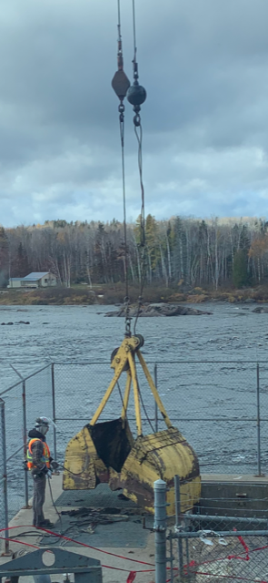 Une grue soulève un grand objet au-dessus d'un plan d'eau.