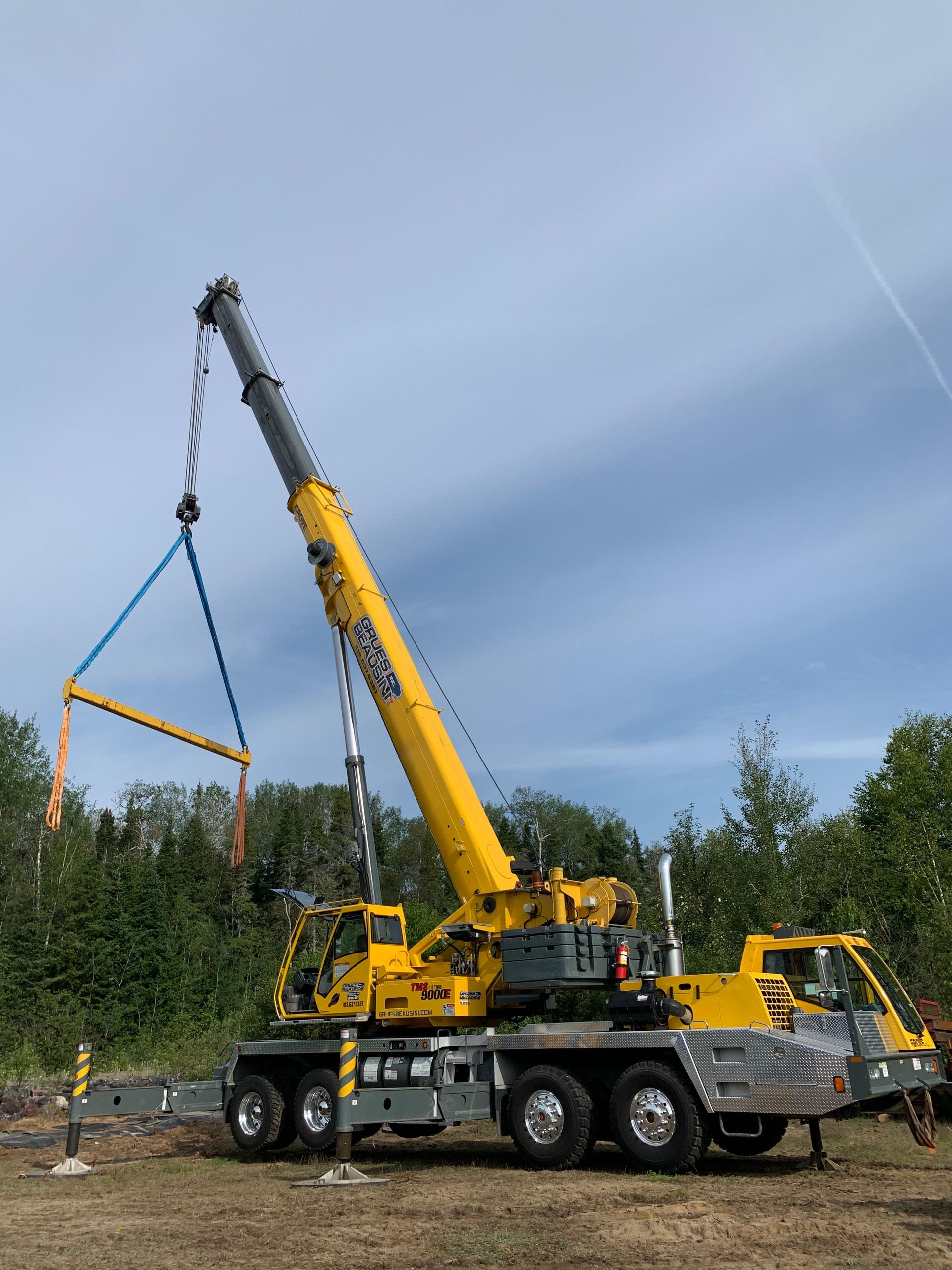 Une grande grue jaune soulève un gros objet dans un champ.