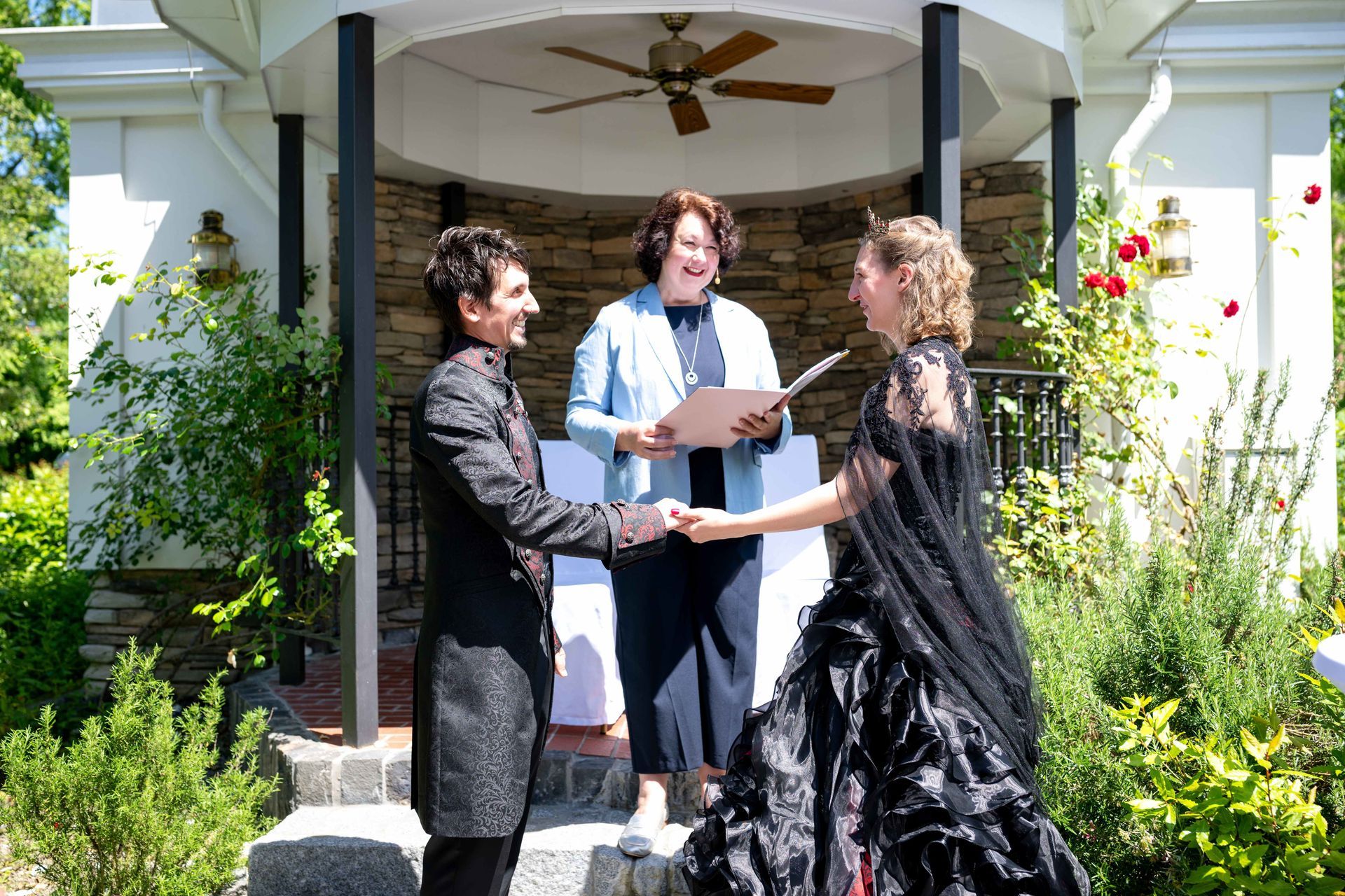 Two people exchange a document with a third person on a porch in bright sunlight.